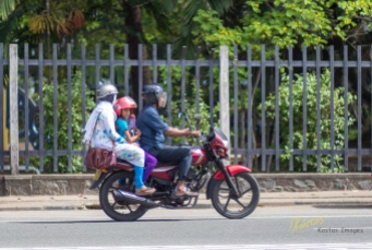 A usual sight in the streets, families (all in helmets) riding motorcycles. The kid was looking at me, although they were under way and I was 50m away from them. Galle, Sri Lanka.
